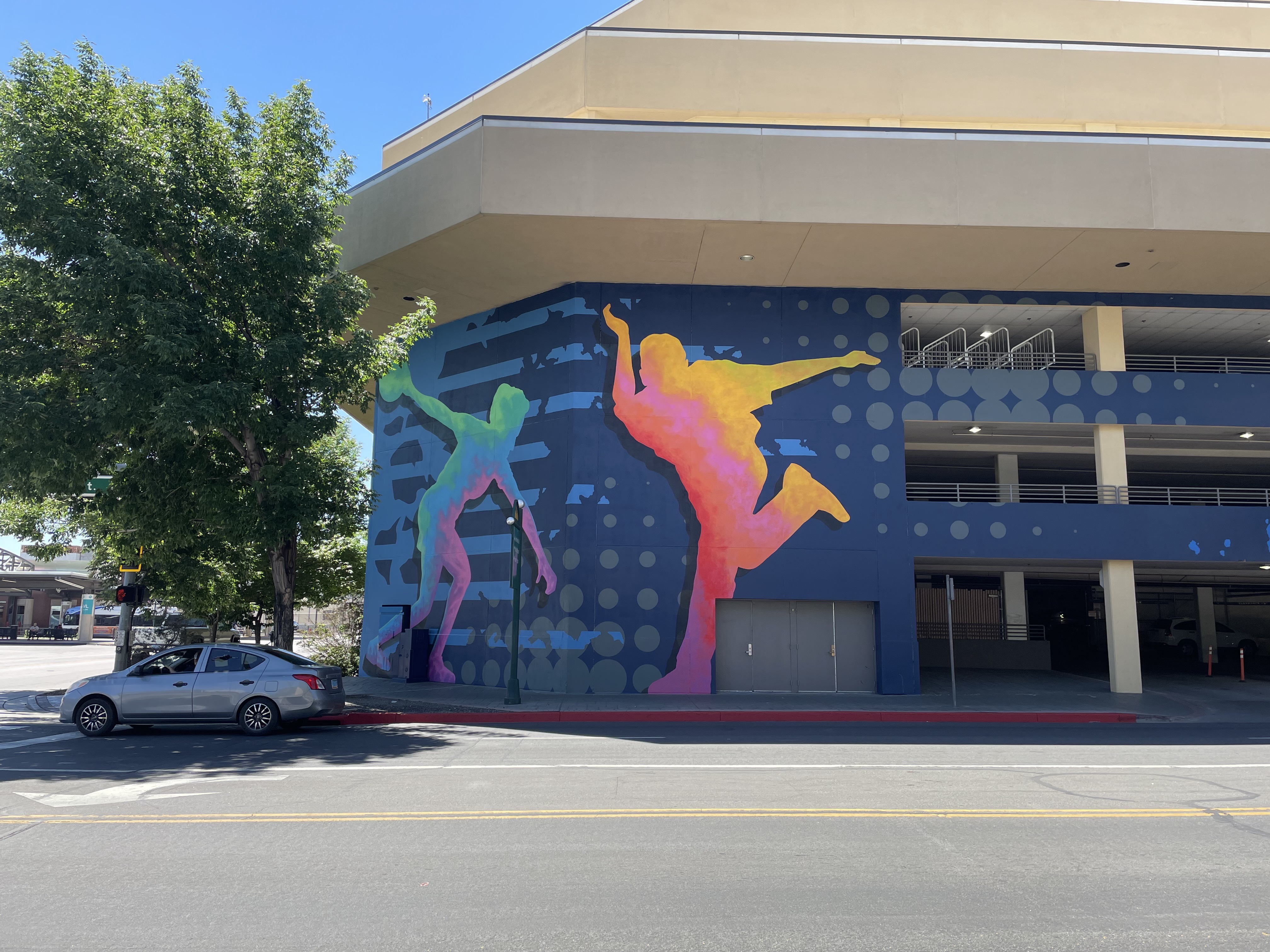 Image of corner of the exterior of a building with a blue patterned background and two figures in bowling poses that appear in green, blue, purple, pink and yellow tones.