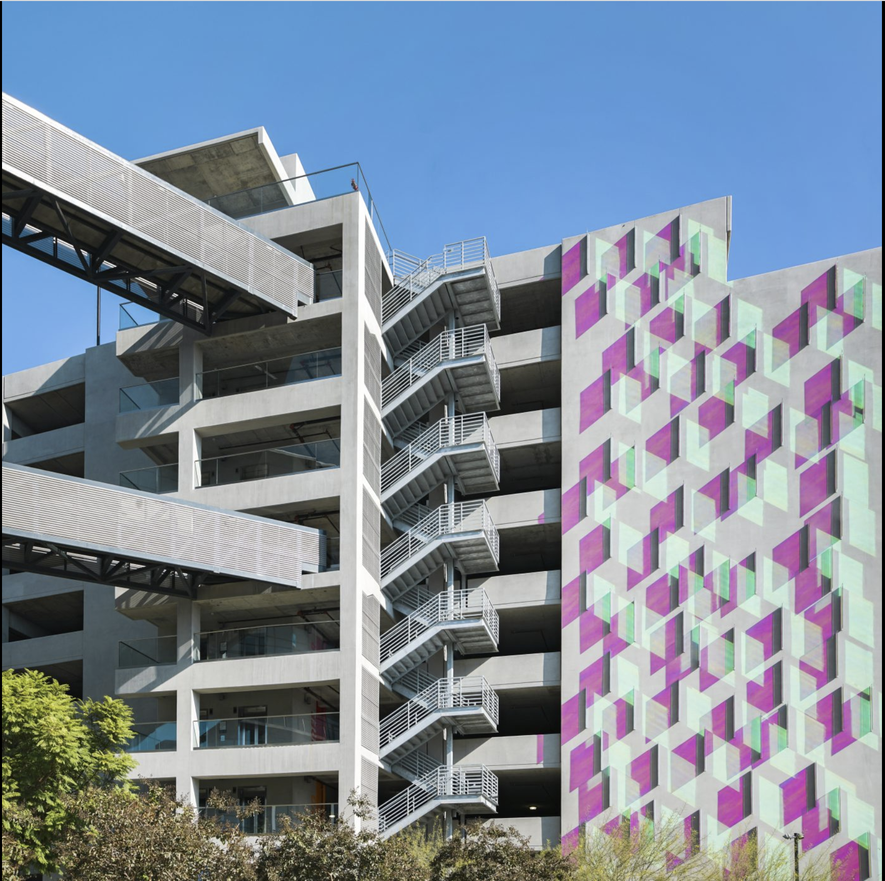 Image of a multi-story parking garage with geometric patterns in purple, green, and white hues that are placed along the exterior of the parking garage.