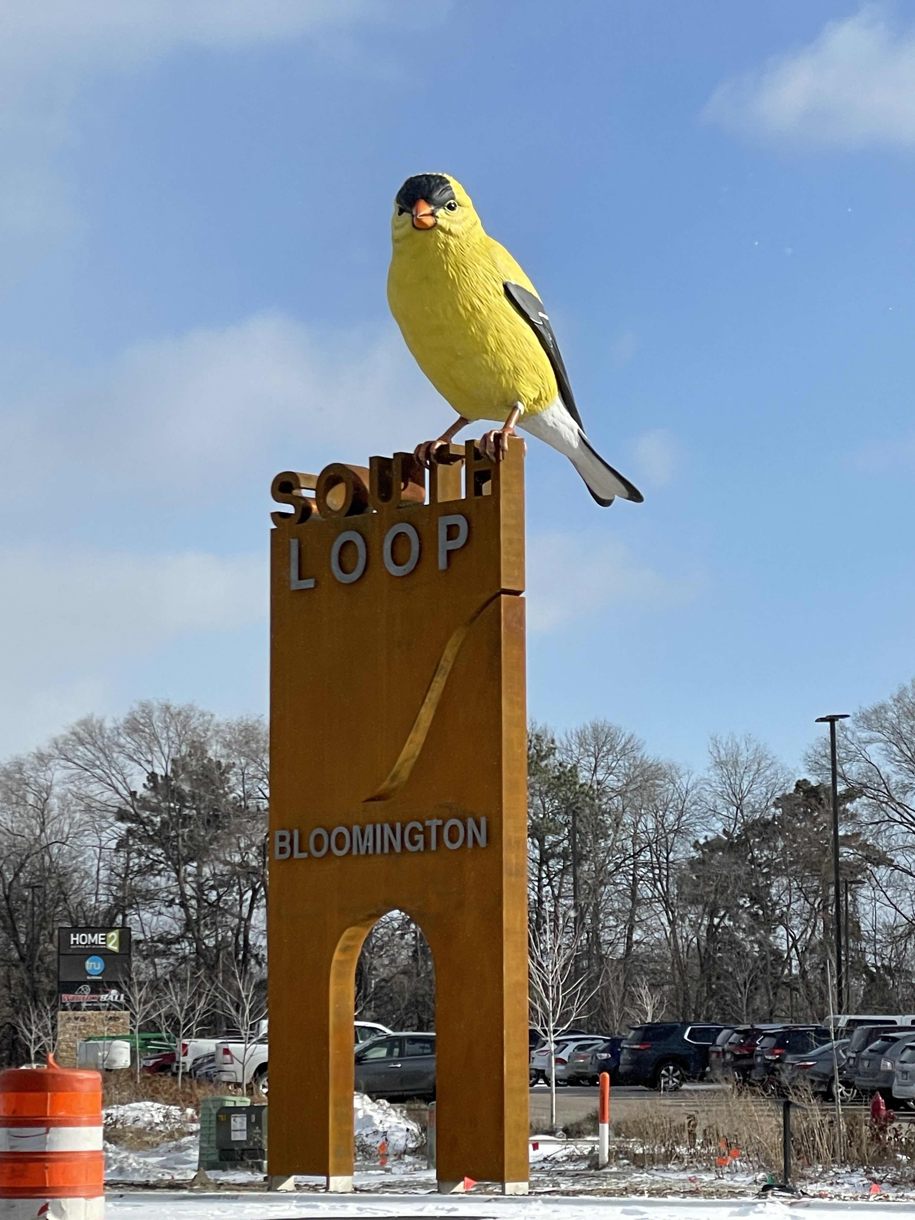 A large yellow bird is perched atop of a large sign that reads Loop with the word Bloomington below.