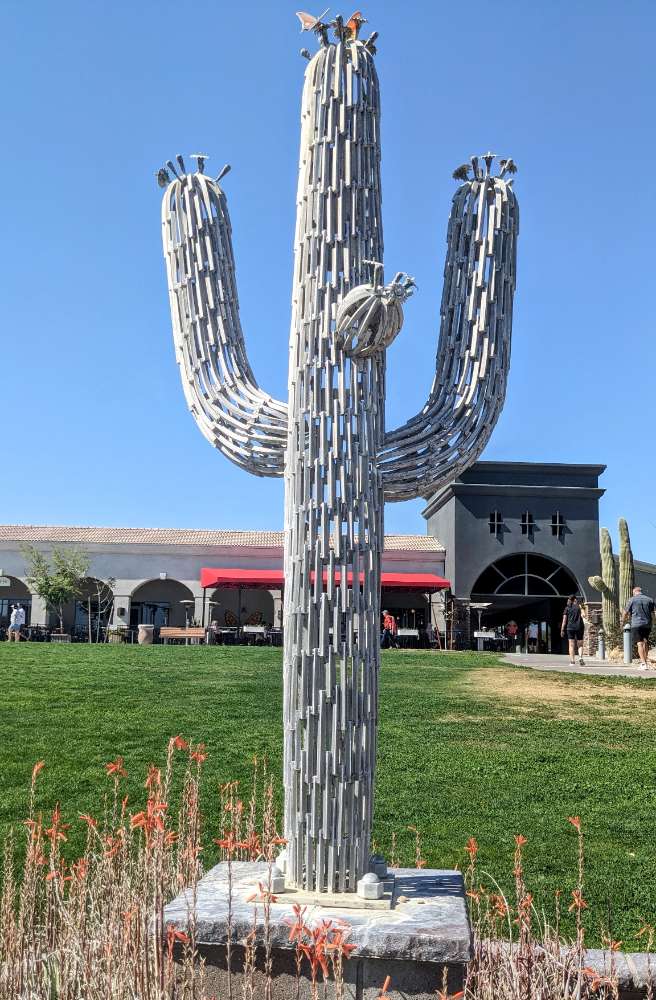 Photograph of a sculpture in the shape of a saguaro cactus on a base placed in a green field.
