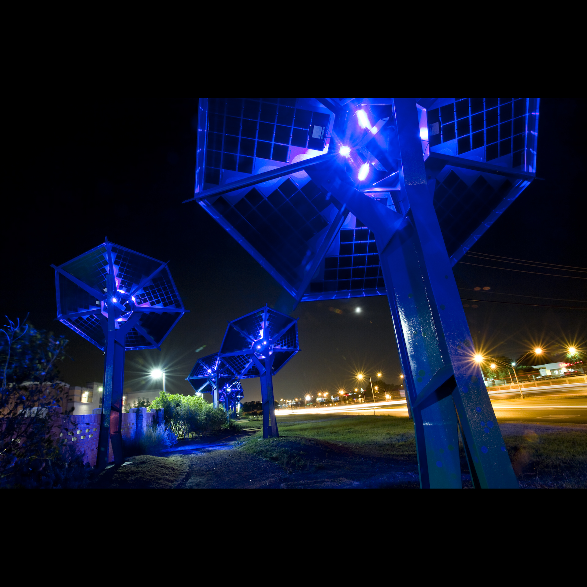 Several florescent blue light posts are placed outside by a highway.