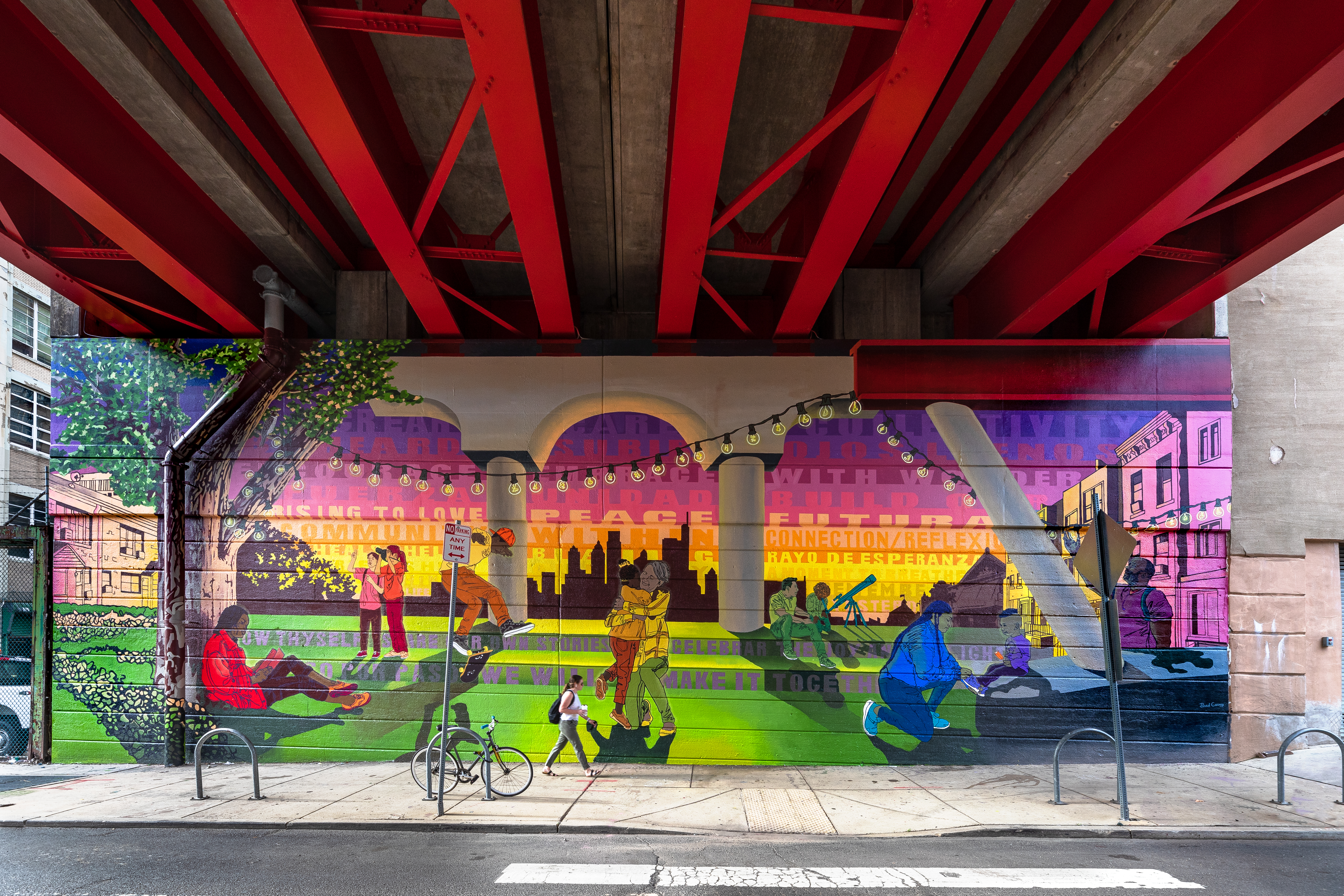 Image of colorful mural under overpass. Mural depicts a diverse group of people reading, dancing, and hanging out in a park under the sunset.