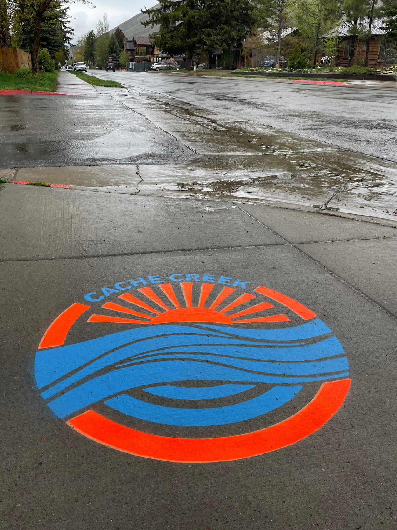 Image of circle shape intersected with blue raves and red sun painted on concrete sidewalk with text that reads Cache Creek.