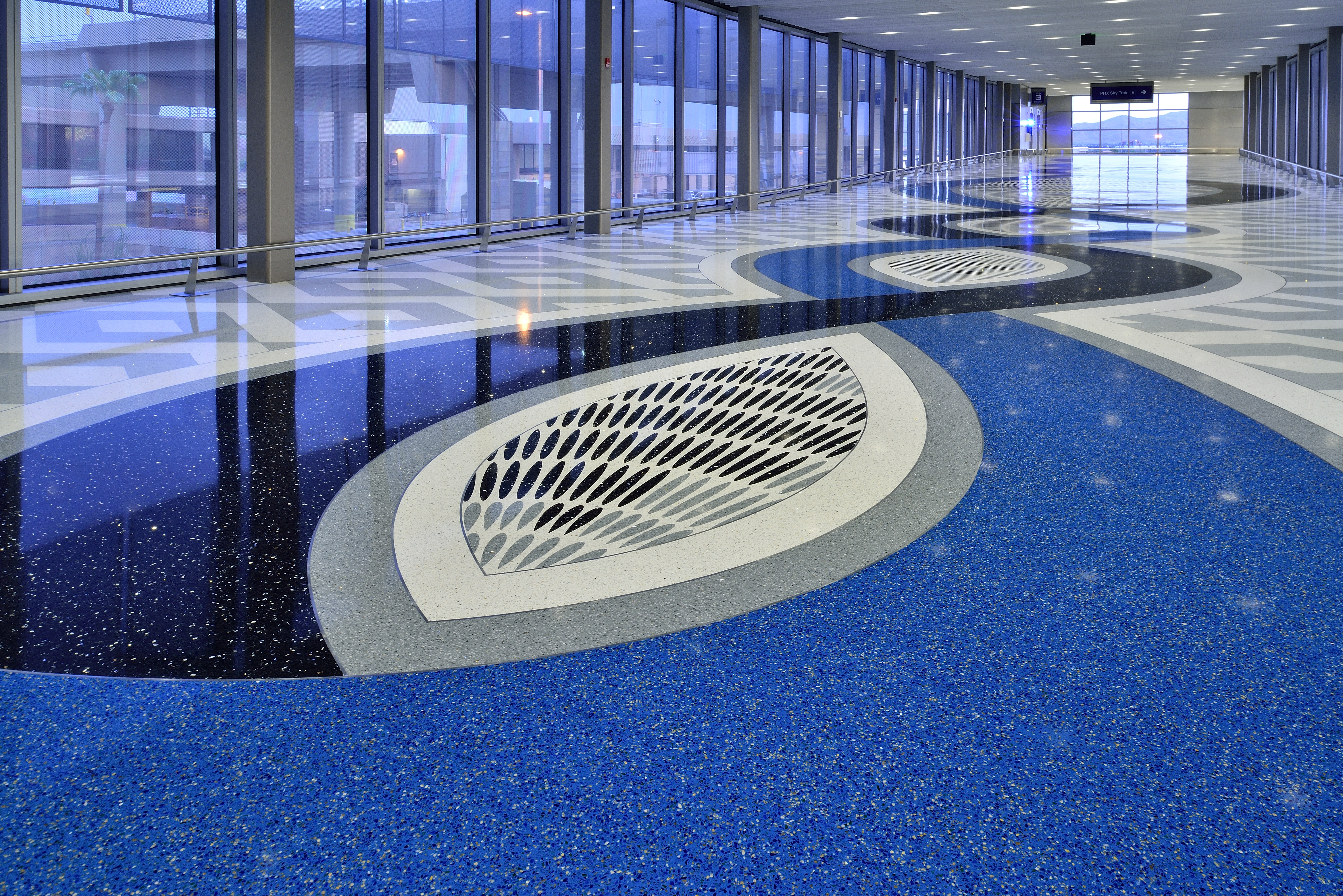Blue terrazzo floor that spans airport corridor with eye-shaped interweaving patterns in dark blue, gray, and white details