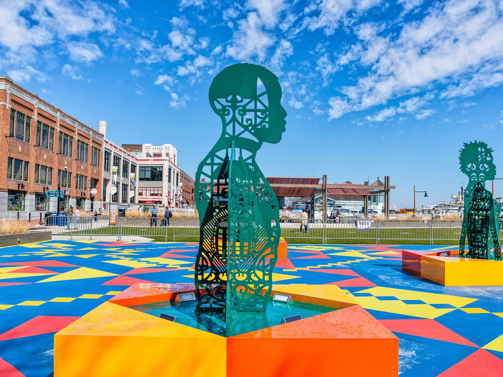 A large dark green sculpture of a man's upper body is placed outside on top of a colorful block.
